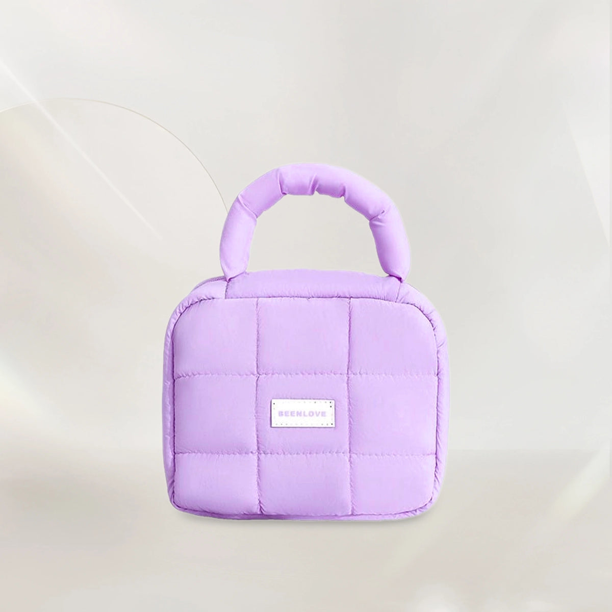 Light purple quilted makeup bag with handle on soft neutral background