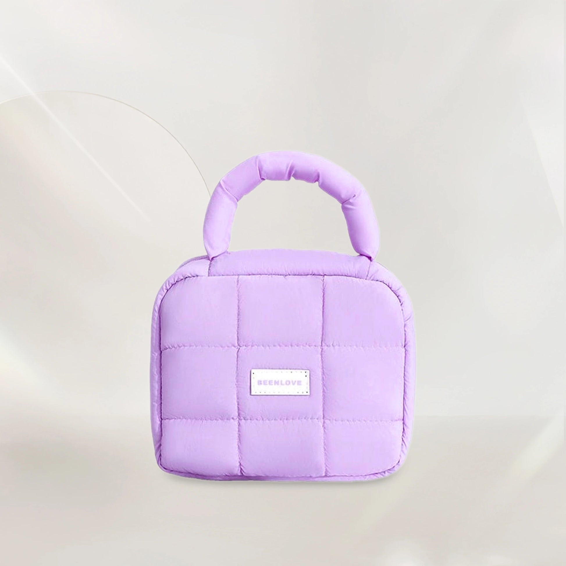 Light purple quilted makeup bag with handle on soft neutral background